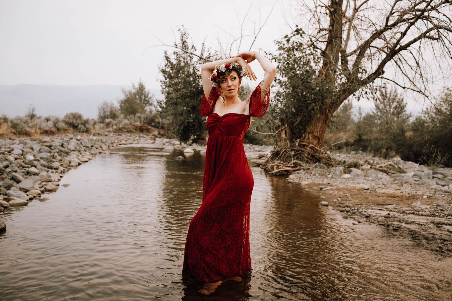 Dramatic river photoshoot featuring burgundy dress and expressive pose in flowing water.