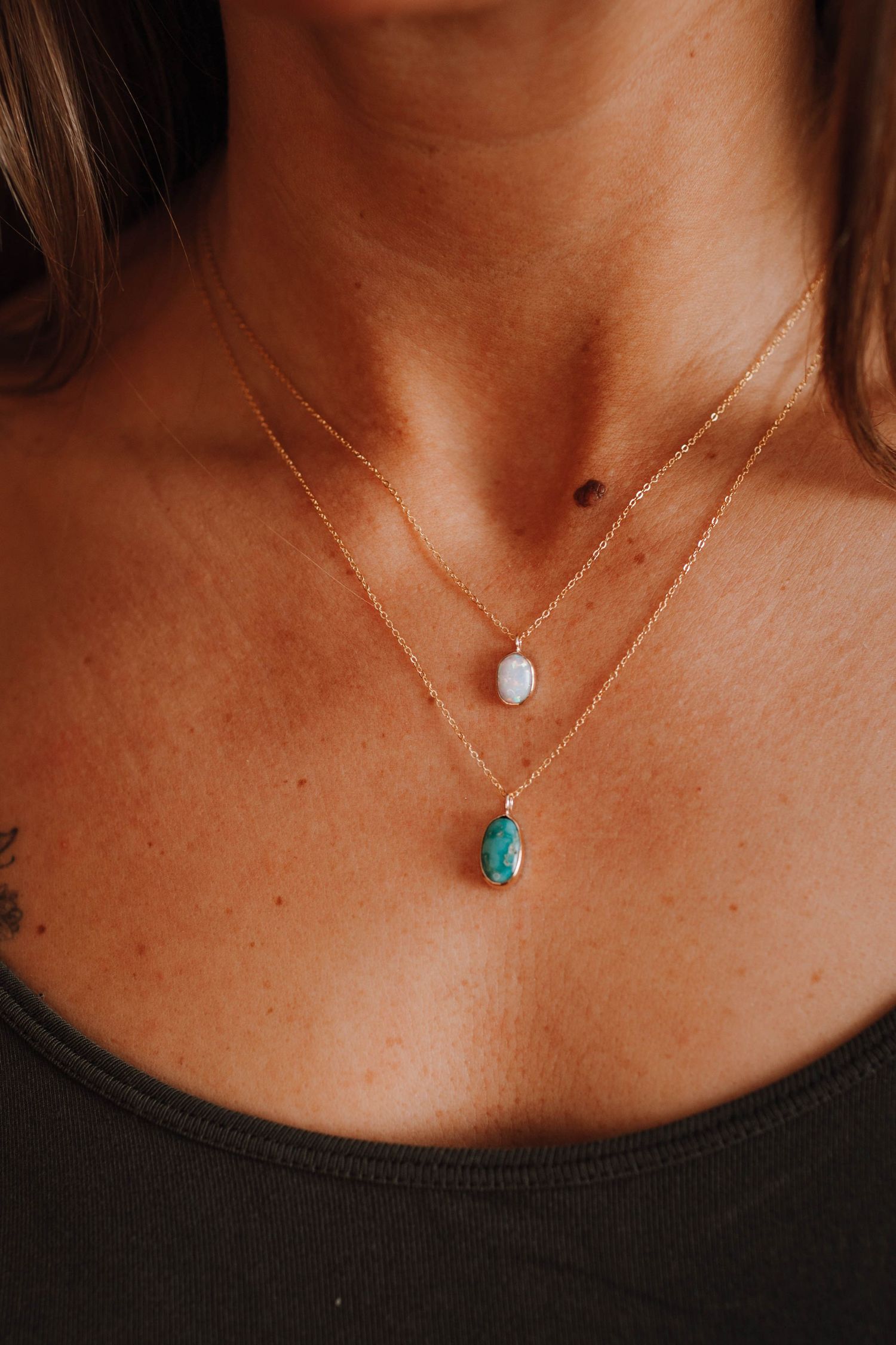 Layered necklaces featuring a white pendant and turquoise stone against dark clothing.