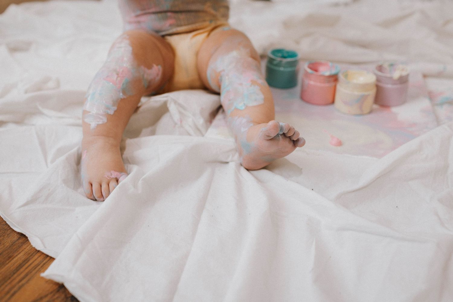 Paint-covered legs and feet on white fabric with colorful paint containers visible.
