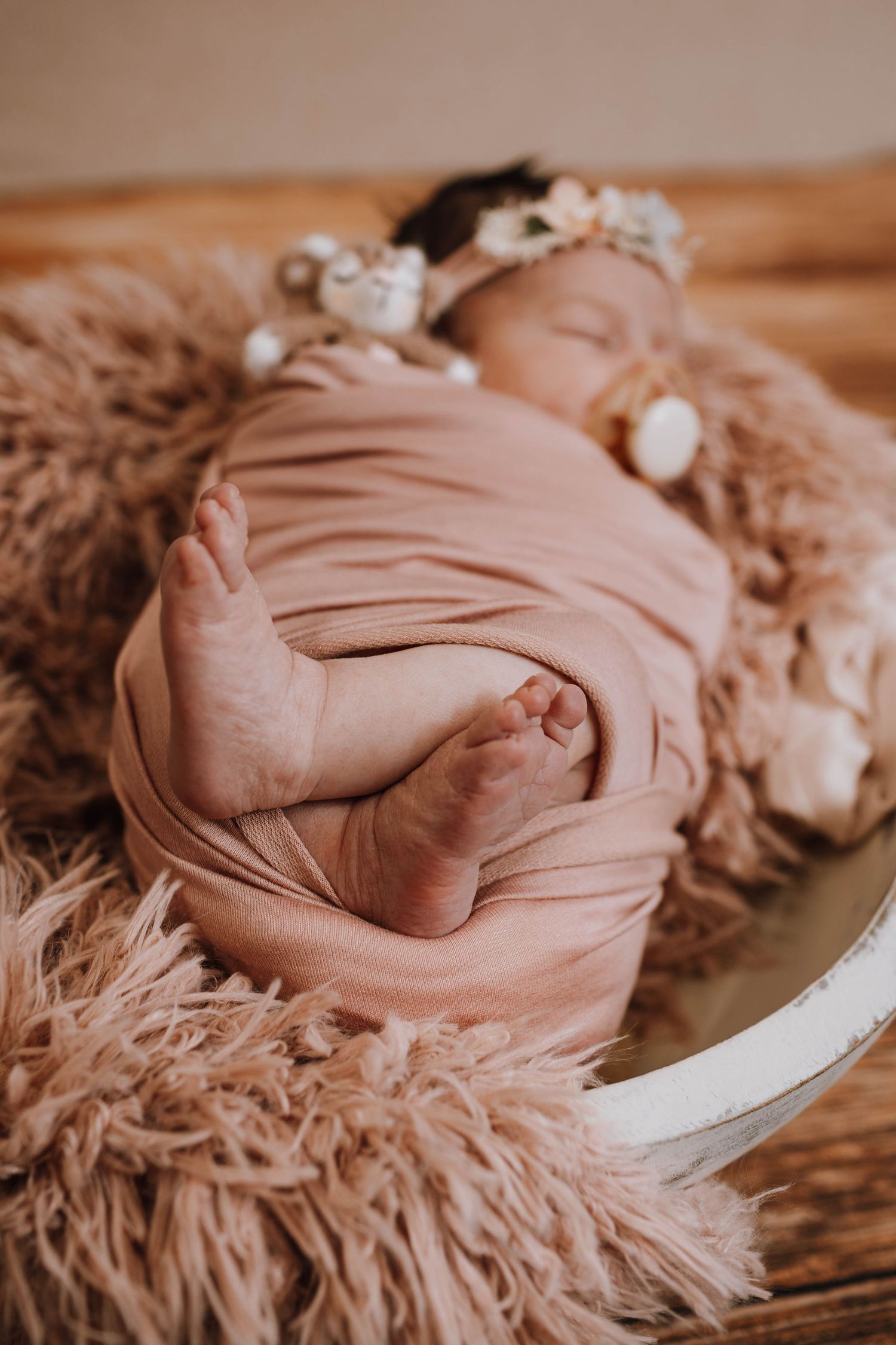Newborn baby sleeping peacefully wrapped in pink fabric on fluffy brown fur.