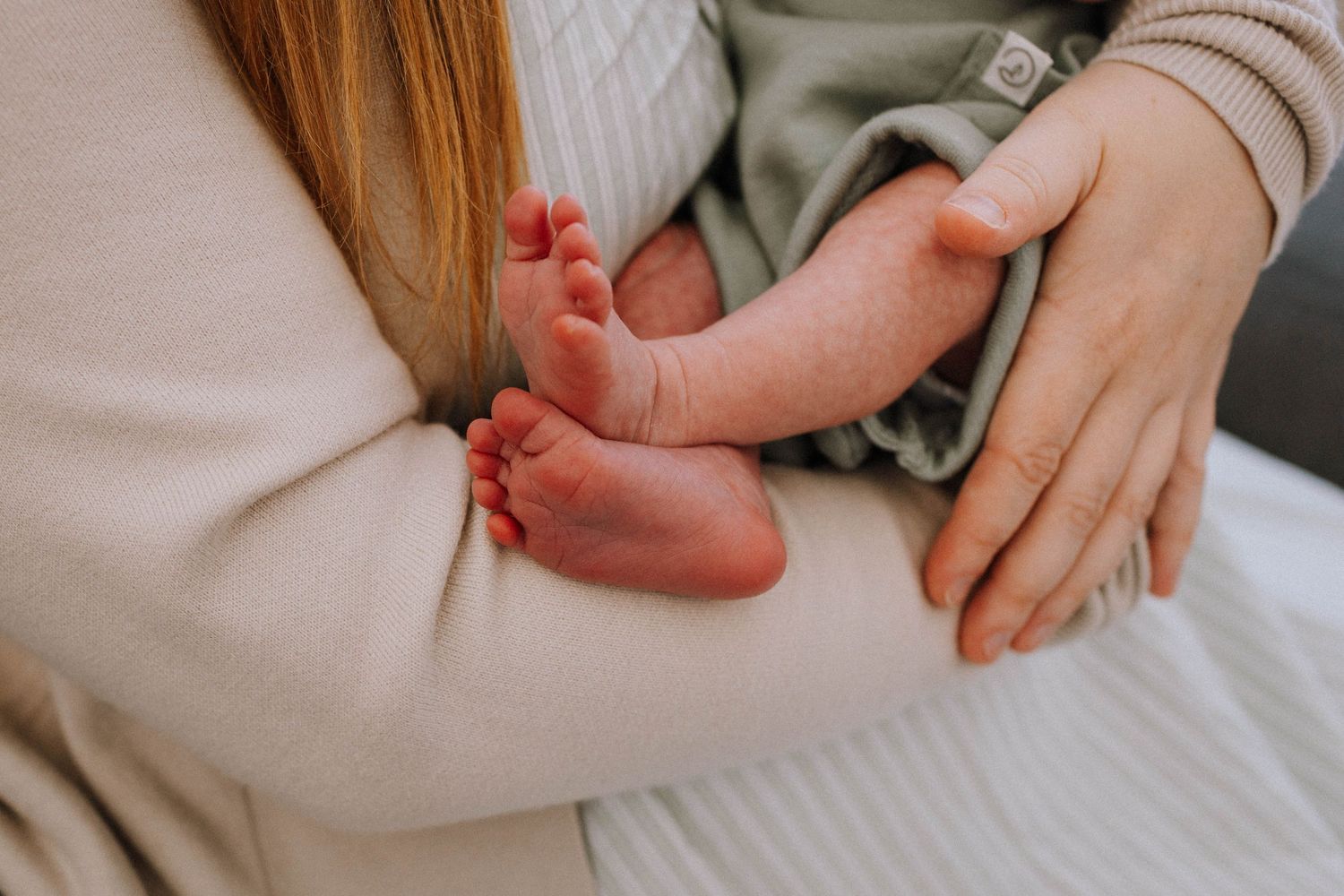 Close up view of tiny newborn baby feet being gently held against soft beige knit fabric.
