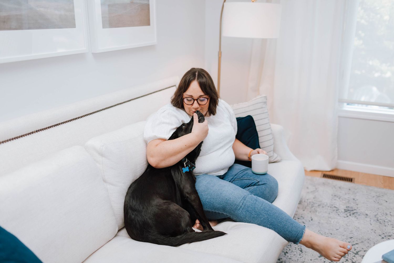 A comfortable home scene showing someone cuddling with a black cat on a white sofa.
