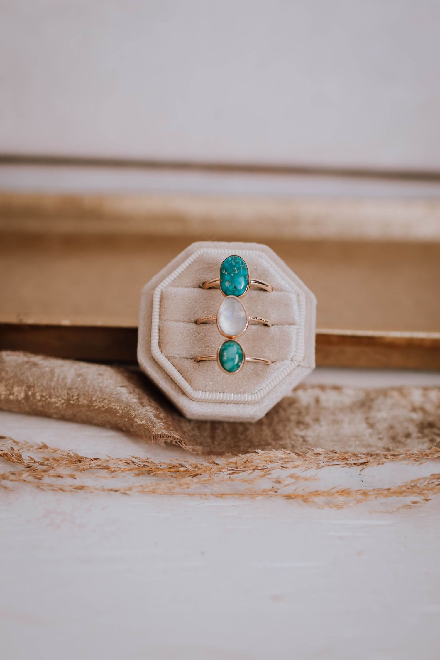 Two vintage turquoise gemstone rings displayed in a white octagonal ring holder against a textured beige surface.