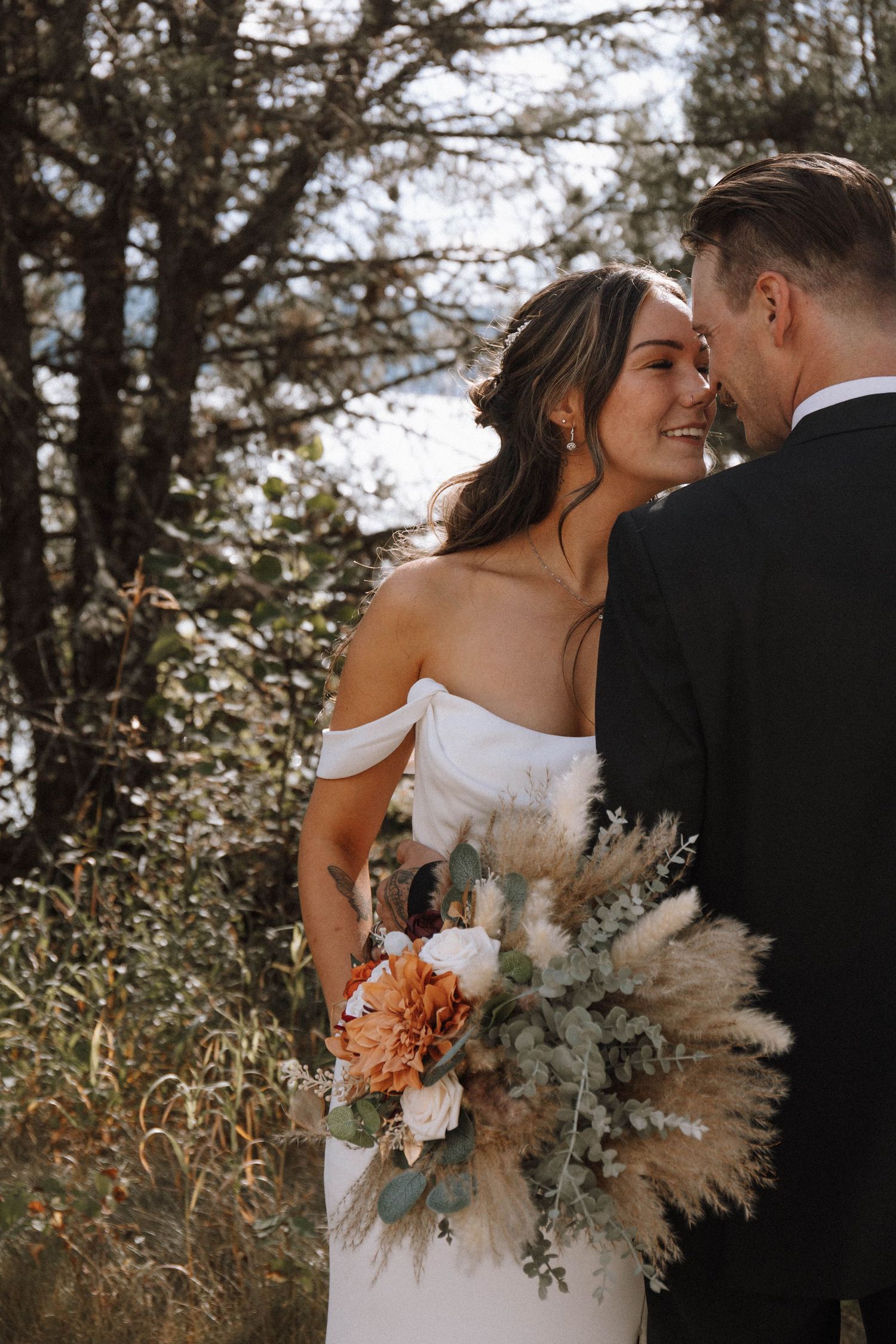 Romantic newlyweds share intimate moments in a forest setting with a beautiful dried floral bouquet featuring pampas grass.