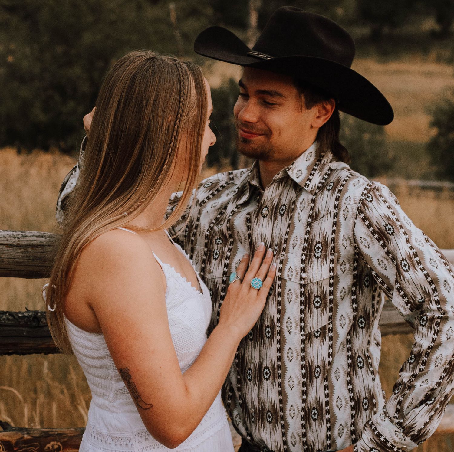 A couple dressed in western attire share an intimate moment against a rustic wooden fence.
