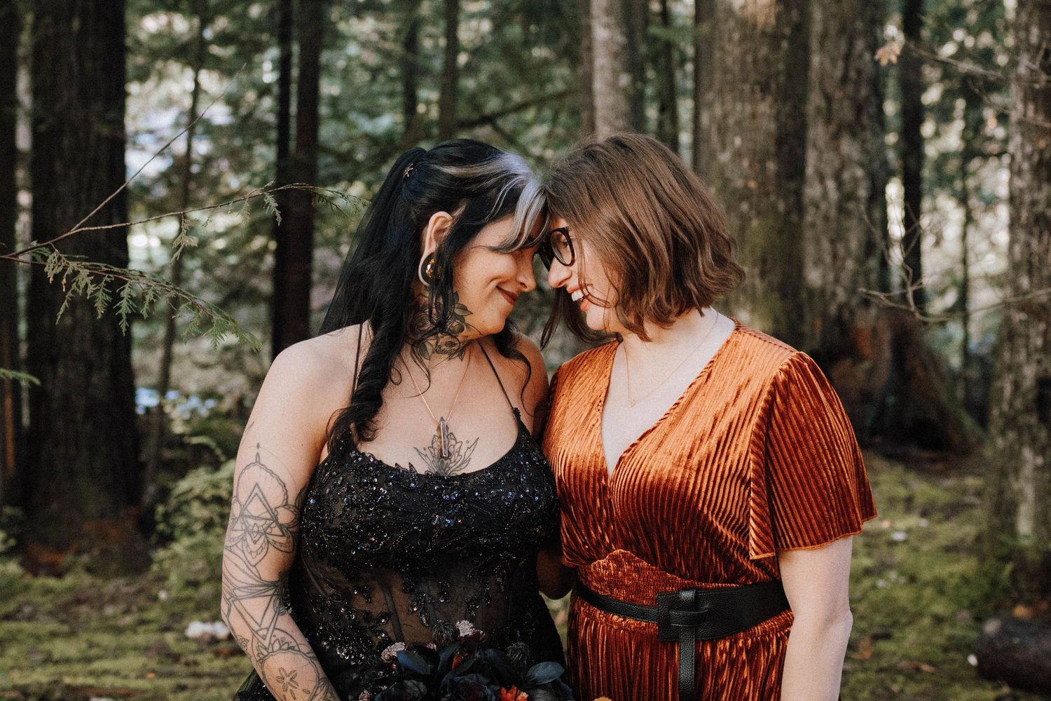 Two people share an intimate moment in a wooded setting wearing contrasting formal attire.