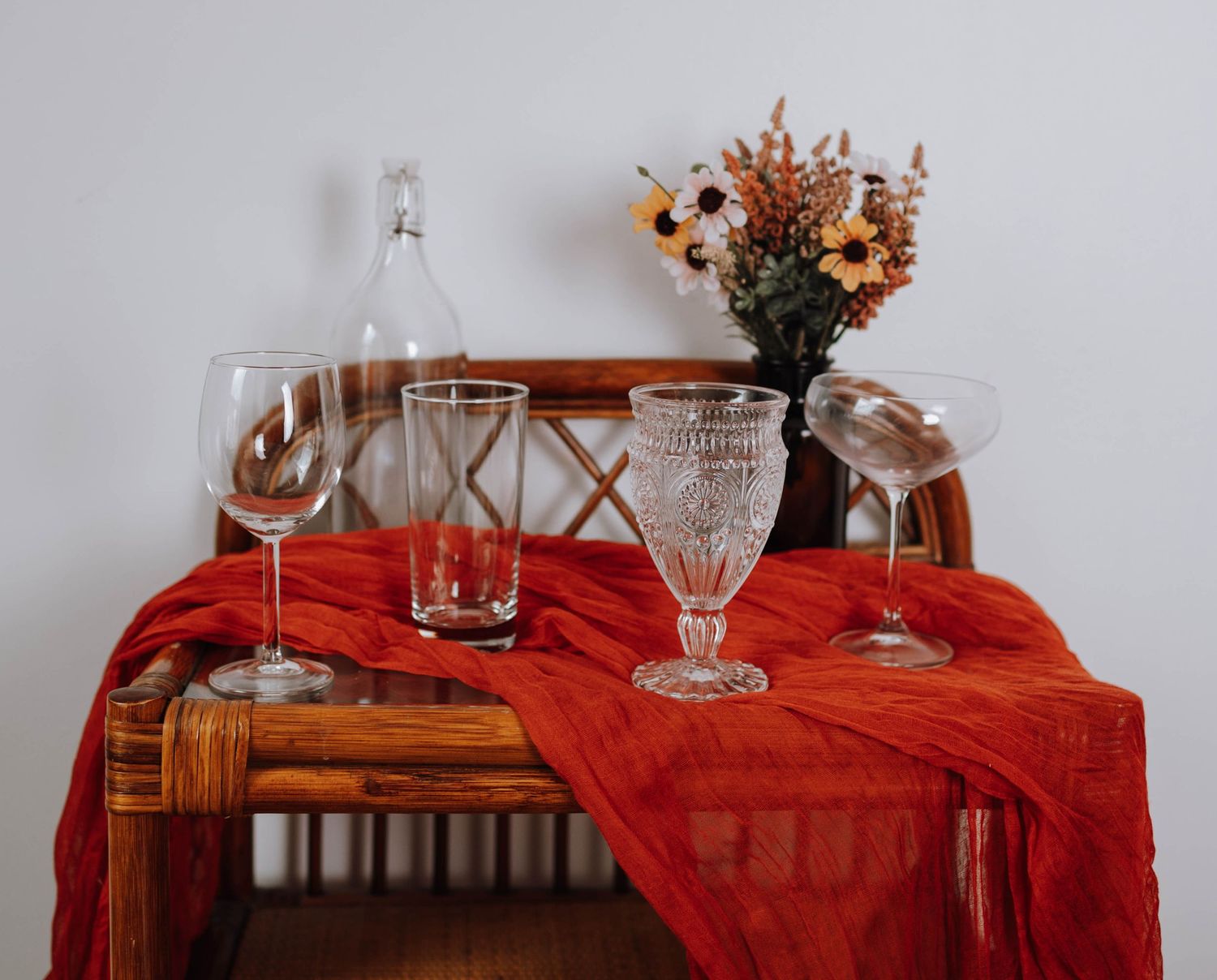 Elegant table setting with crystal glassware and dried flowers on red tablecloth.