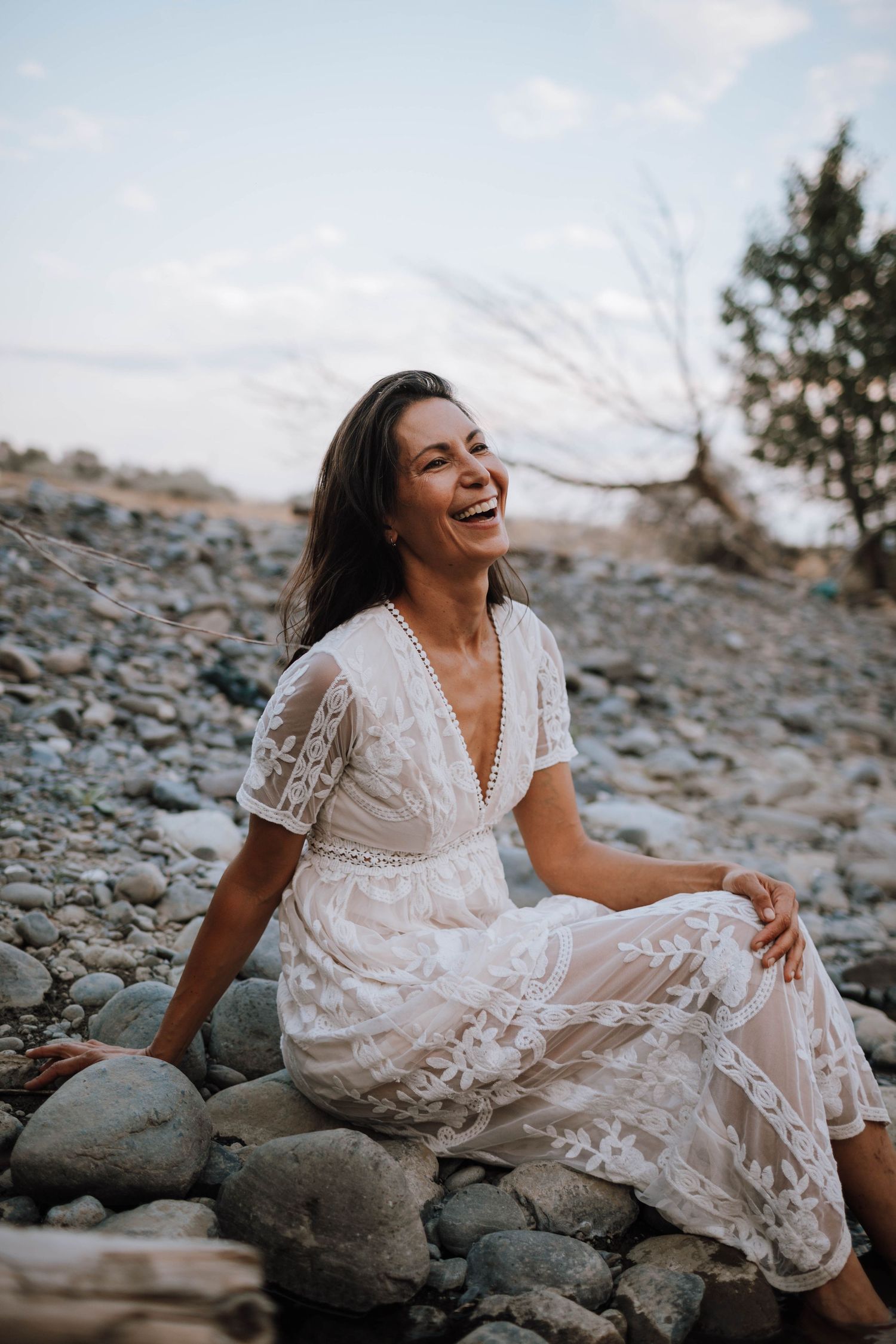 Joyful moment captured on rocky terrain with person in white lace dress during golden hour.