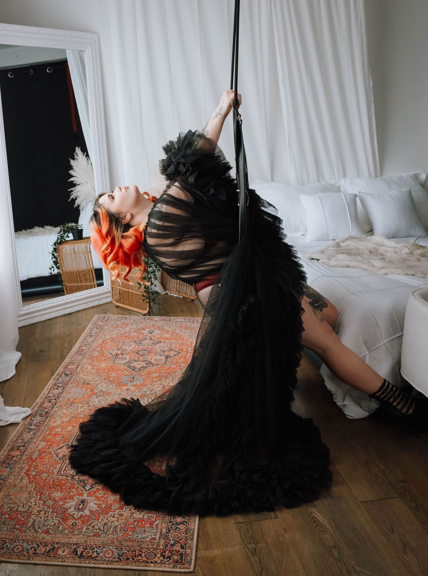 Dramatic pole dance pose with black tulle skirt against white curtain backdrop.