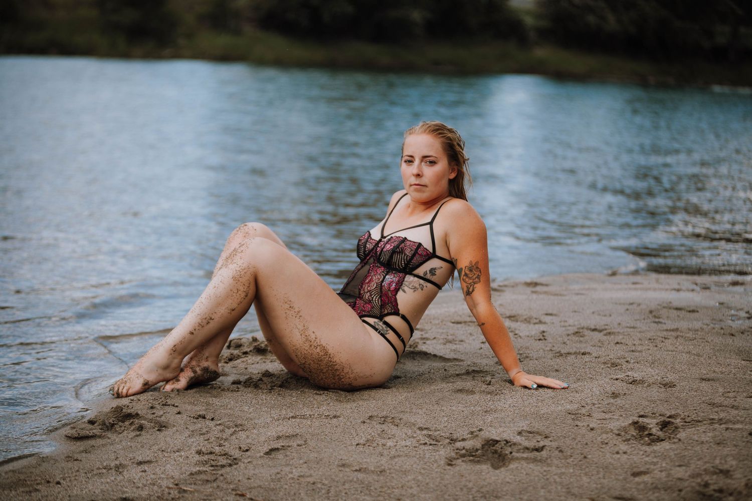 Sensual beach portrait with model in lace lingerie reclining on sand near lake.