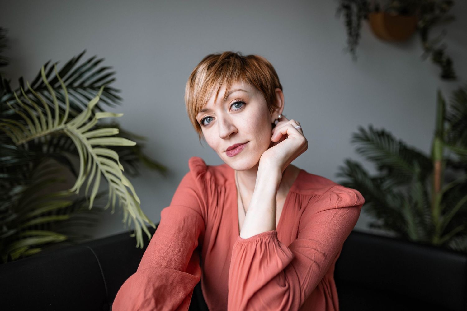 Lifestyle portrait with palm plants featuring person in coral top against grey wall.