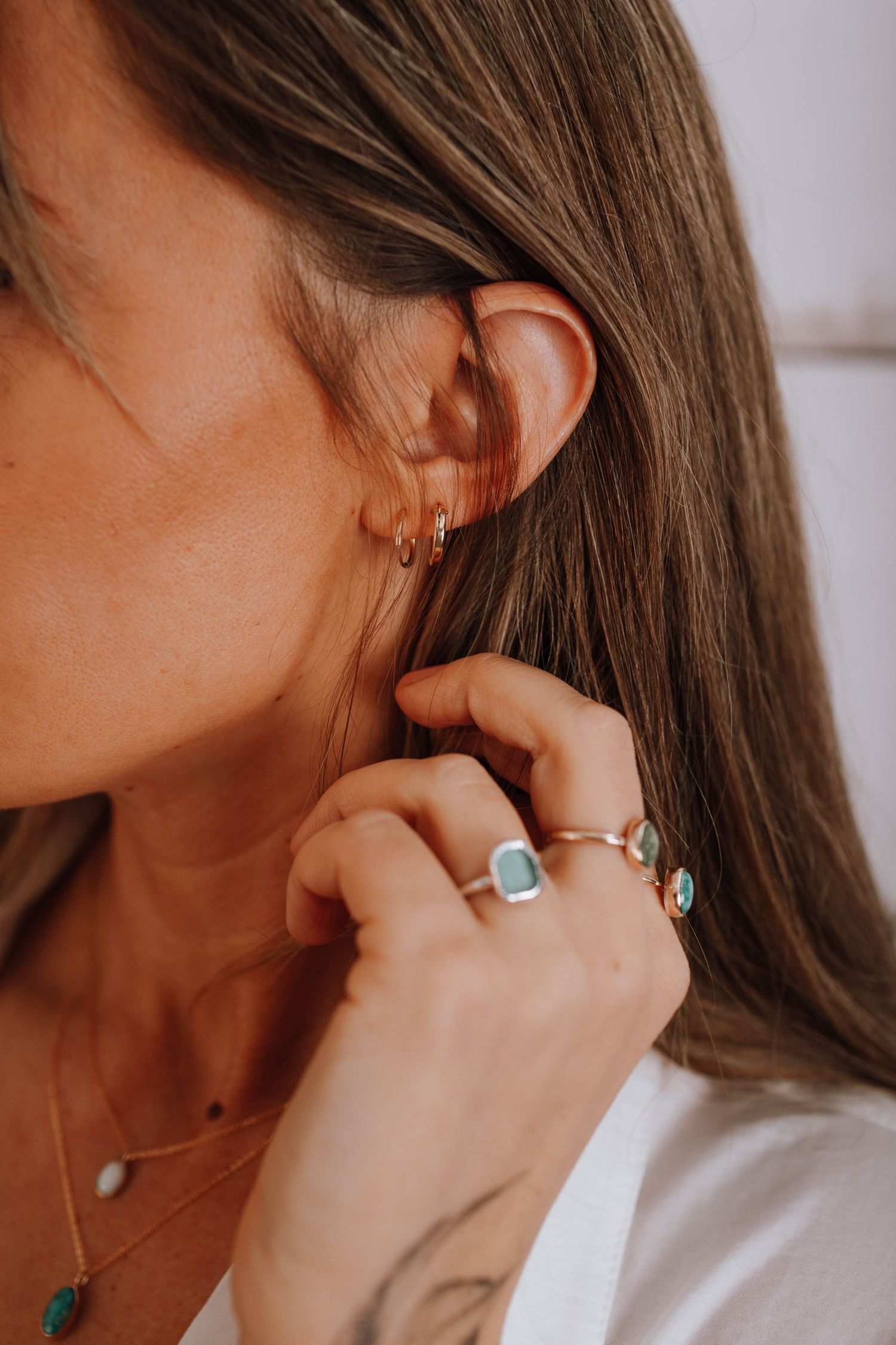 Close-up of multiple ear piercings and turquoise rings against white clothing.