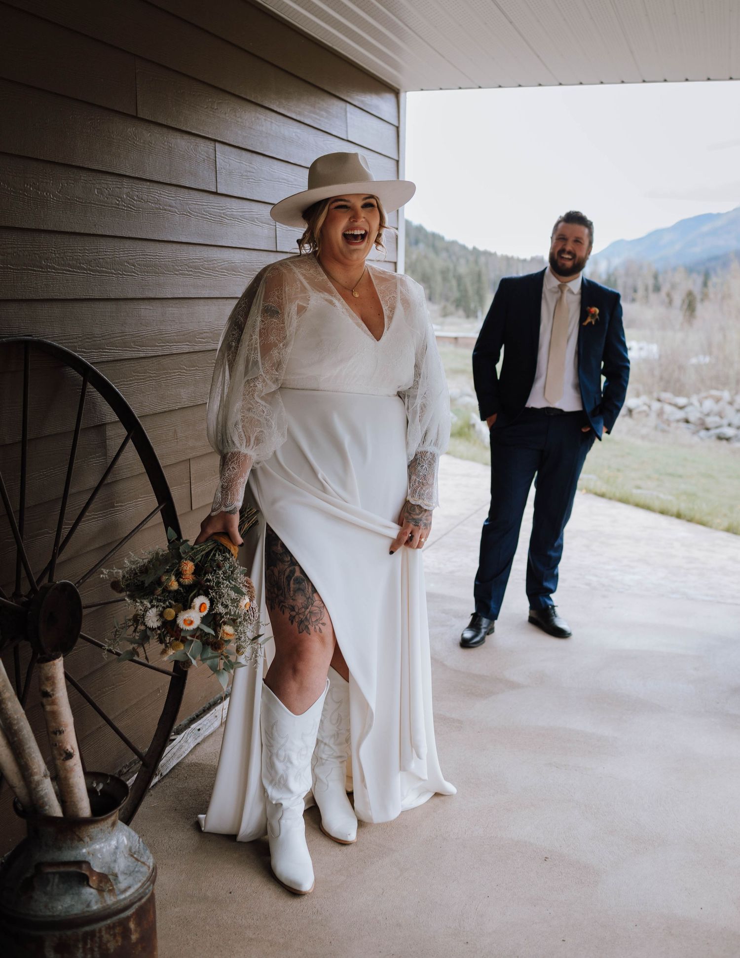 A bride in white dress and cowboy boots poses on a porch with rustic wagon wheel decor.
