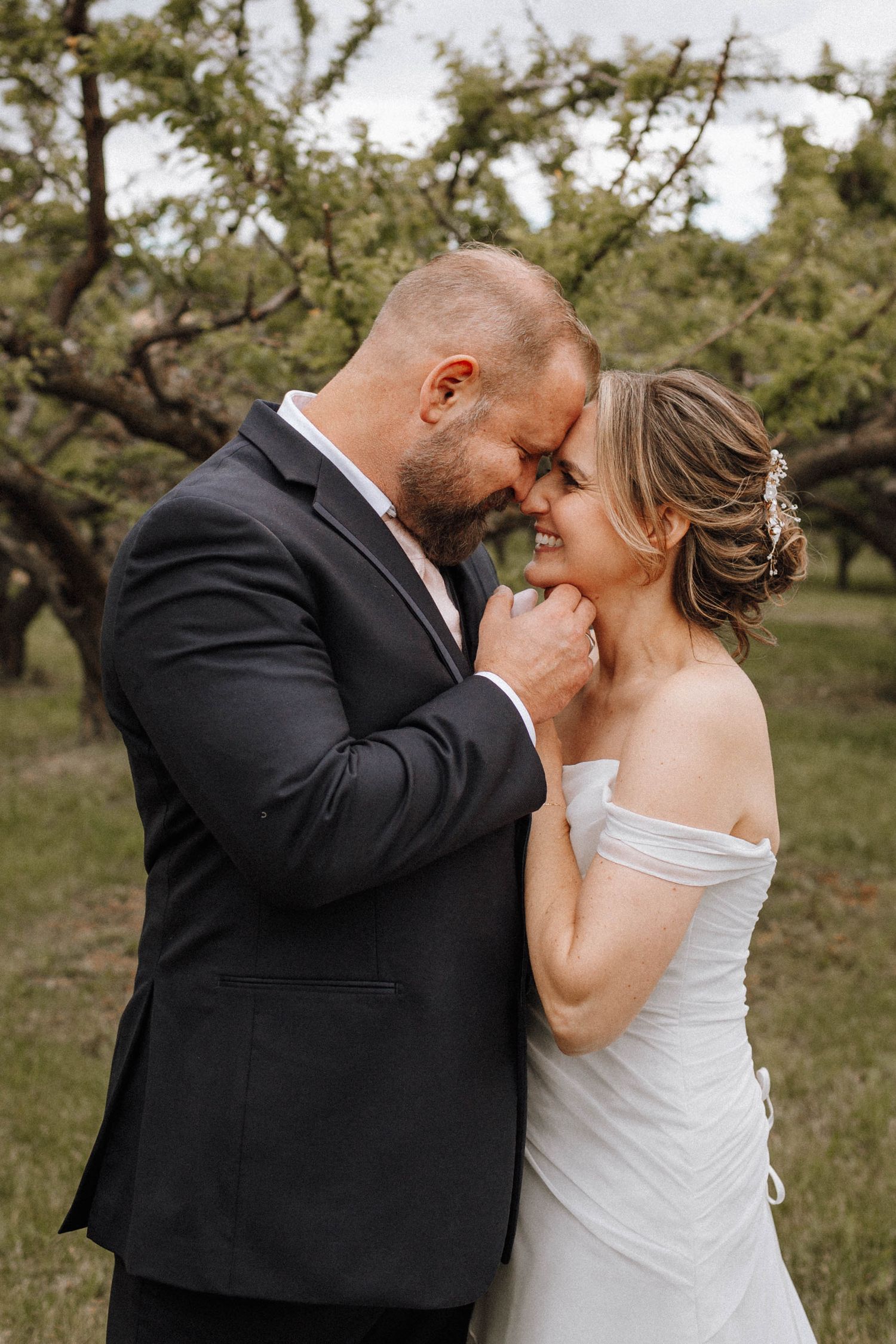 Intimate moment between newlyweds in rustic orchard setting.
