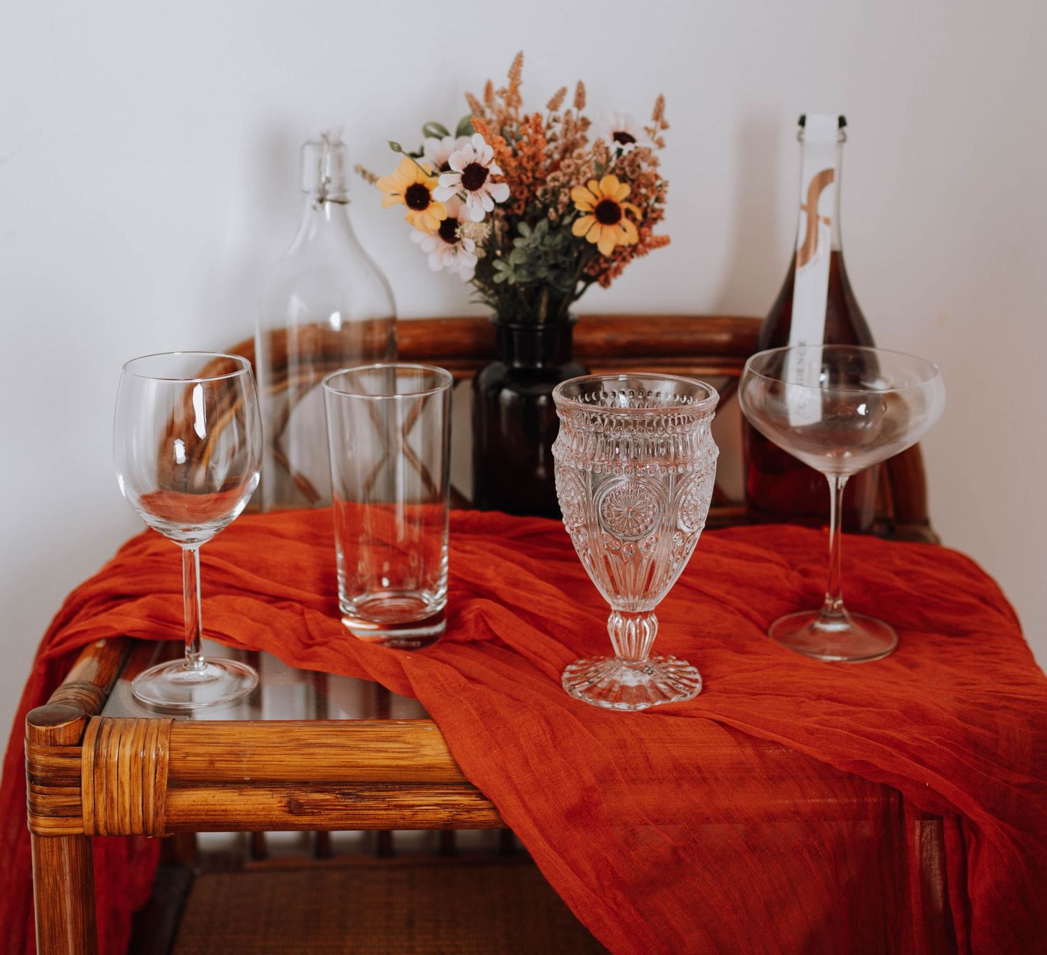 Vintage glassware and dried flowers arranged on a red tablecloth.