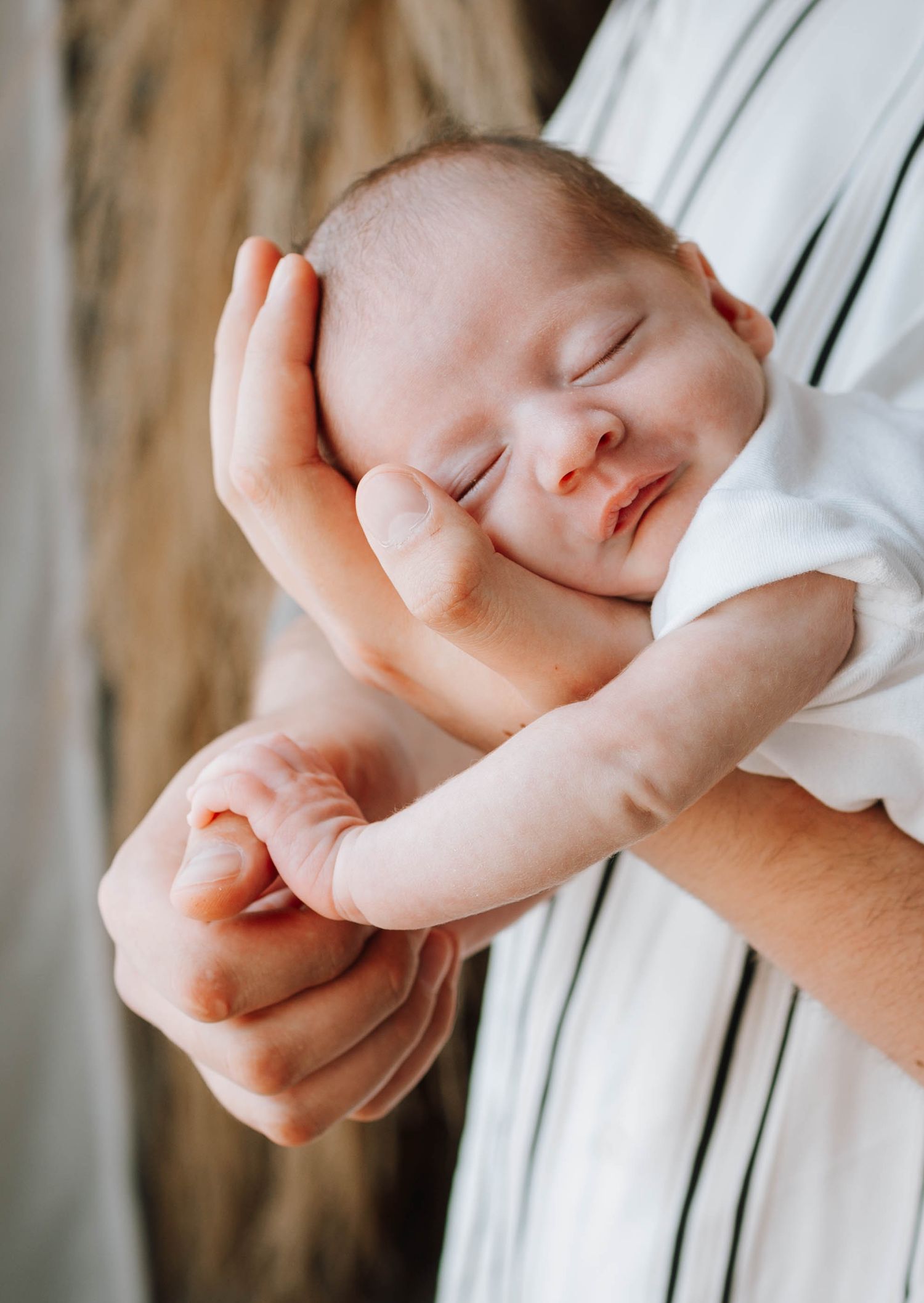 Sleeping newborn cradled in adult hands against white background.