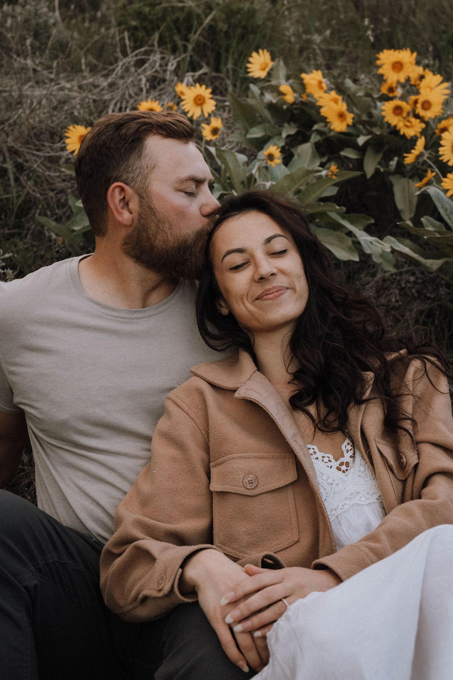 A tender romantic moment captured outdoors with bright sunflowers in the background on a sunny day.