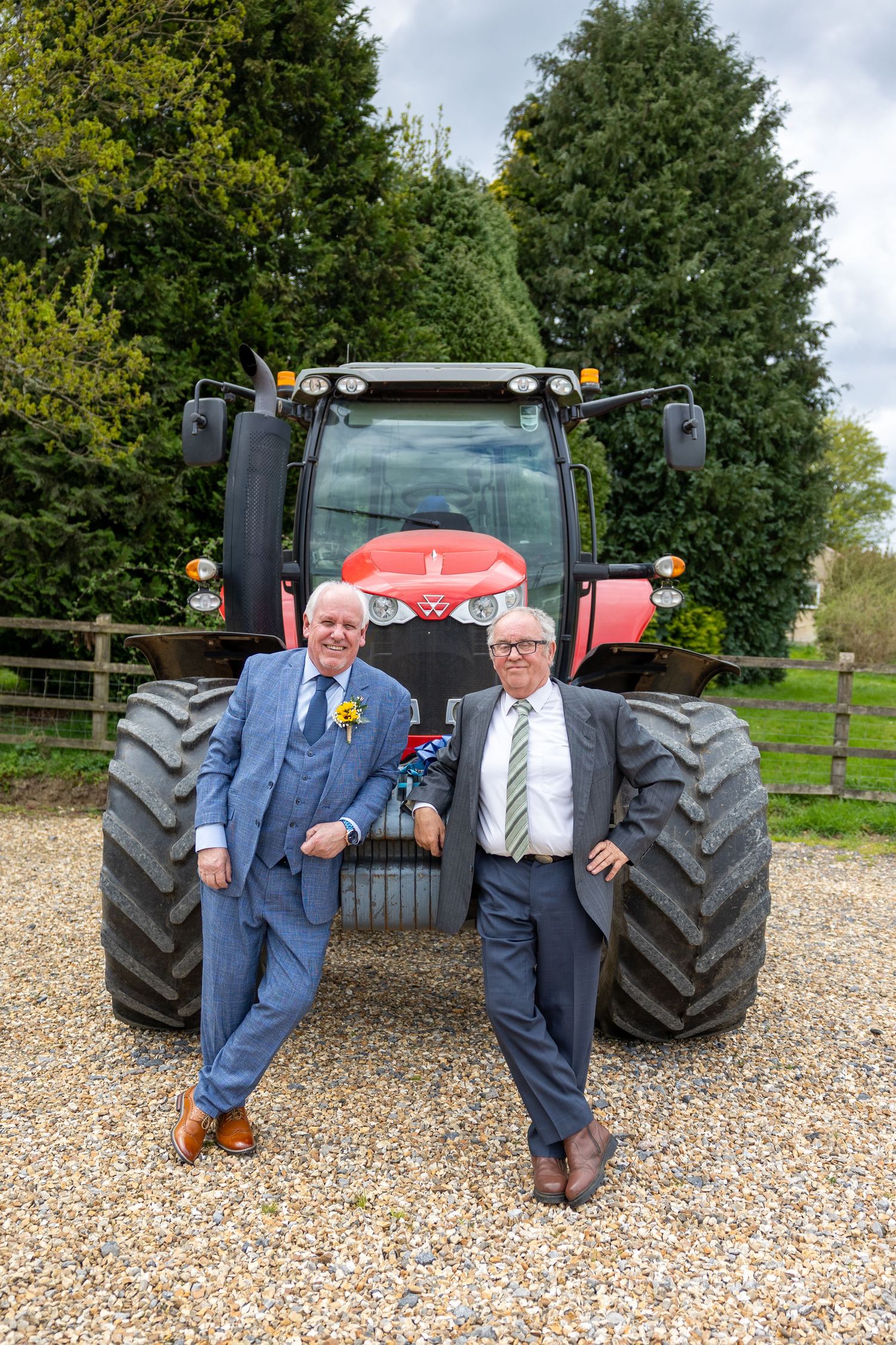 A red Massey Ferguson tractor parked on gravel with mature trees in the background.