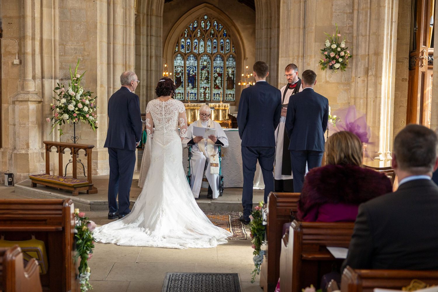 Wedding ceremony in progress inside a beautifully decorated traditional church with flower arrangements.
