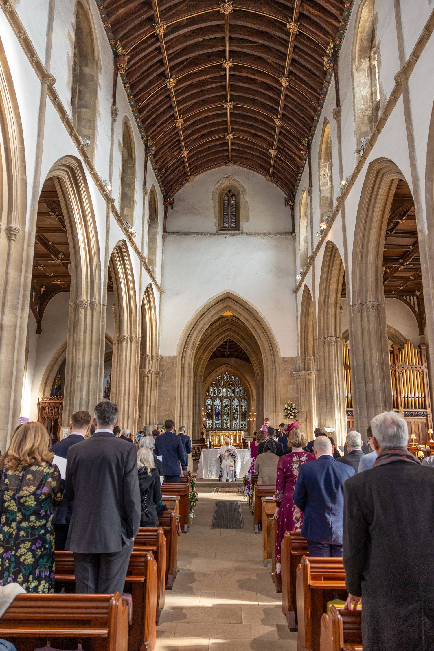 Interior of a grand church with vaulted wooden ceiling and Gothic arches during a wedding ceremony.
