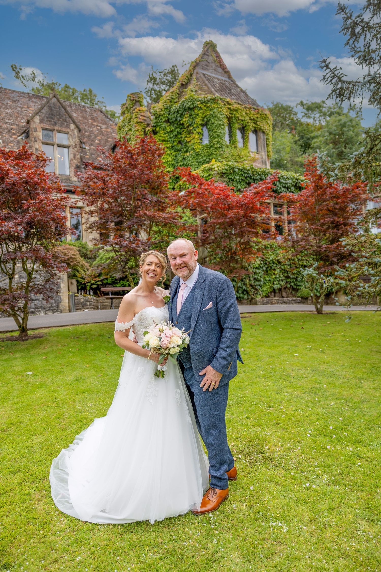 A wedding portrait in front of a historic building with red maple trees and ivy-covered walls.