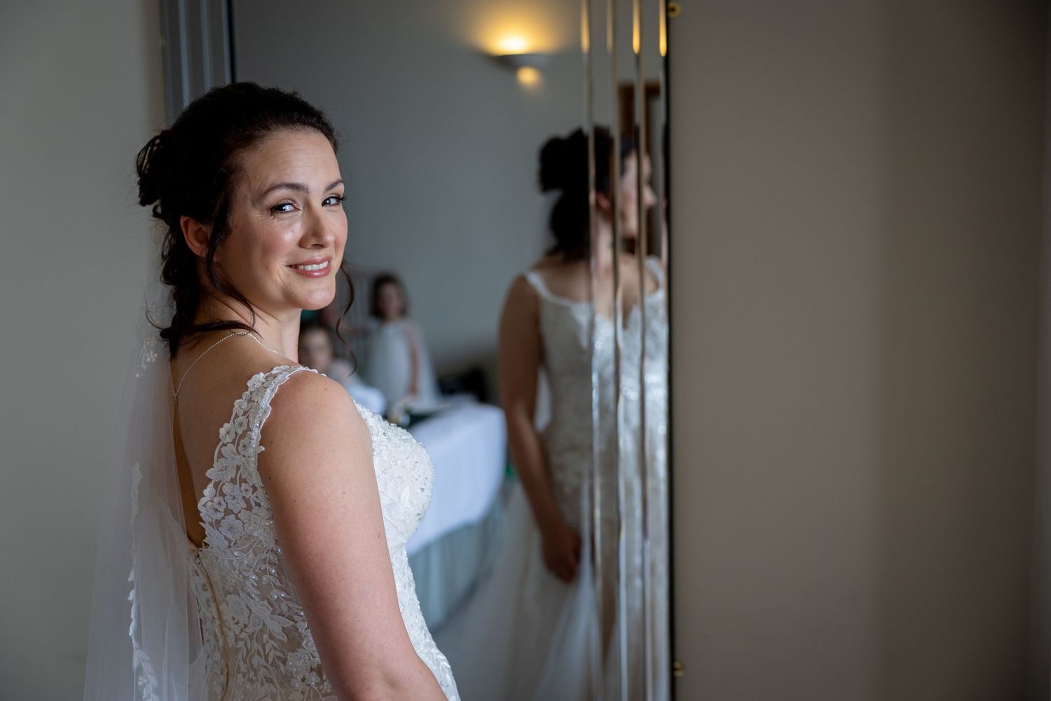 A candid getting-ready moment captured in a mirror reflection showing a wedding dress.