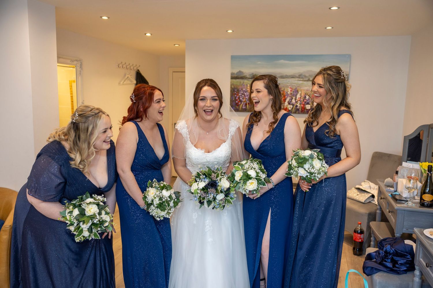 Bridesmaids in navy blue dresses gather with bride holding white and green bouquets.