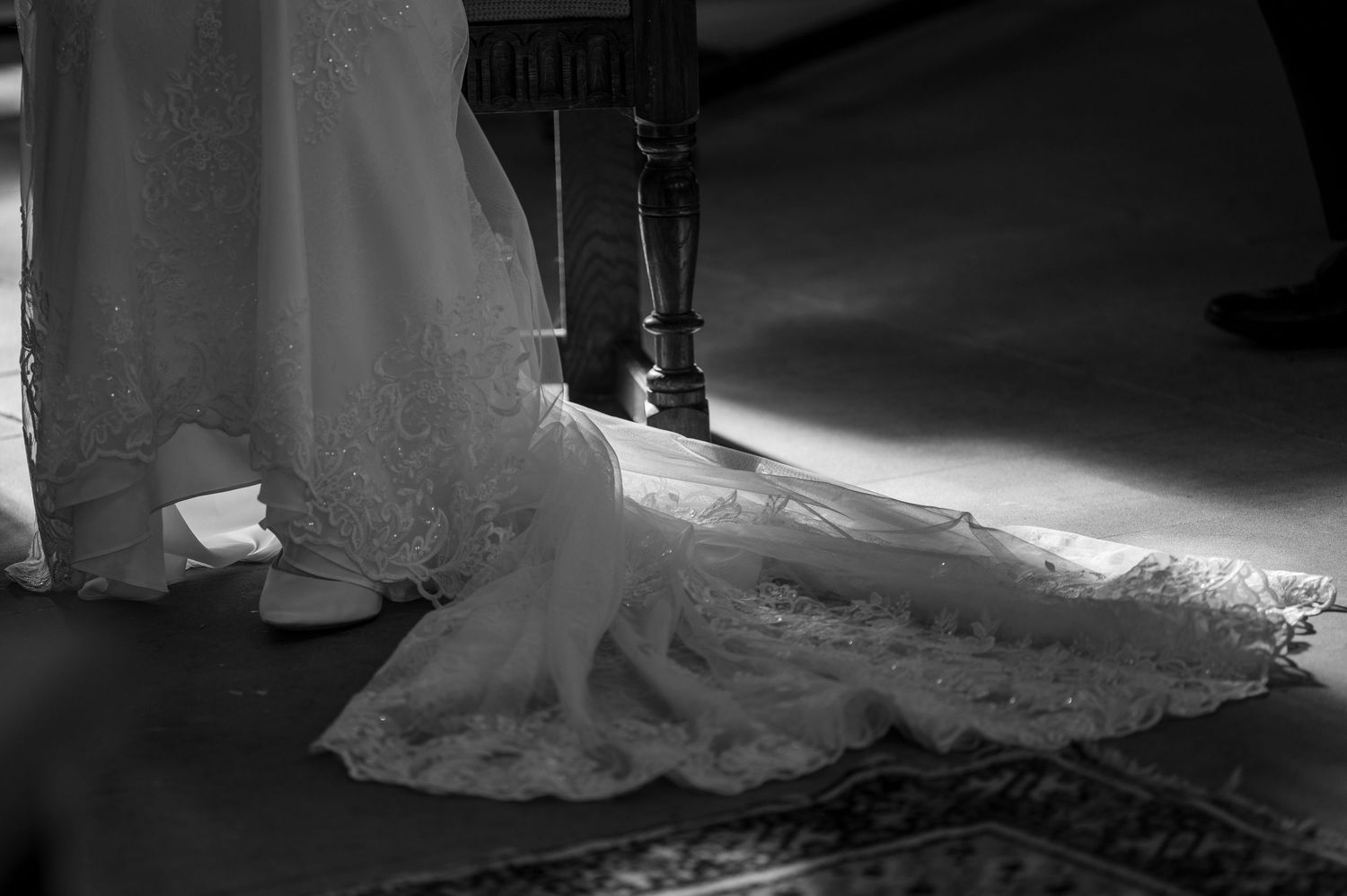Artistic black and white detail of a wedding dress train on stairs.