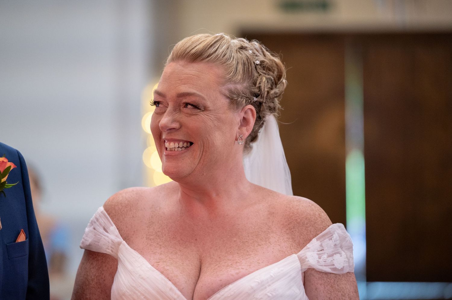 A bride in an off-shoulder white wedding dress smiles brightly during her wedding celebration.