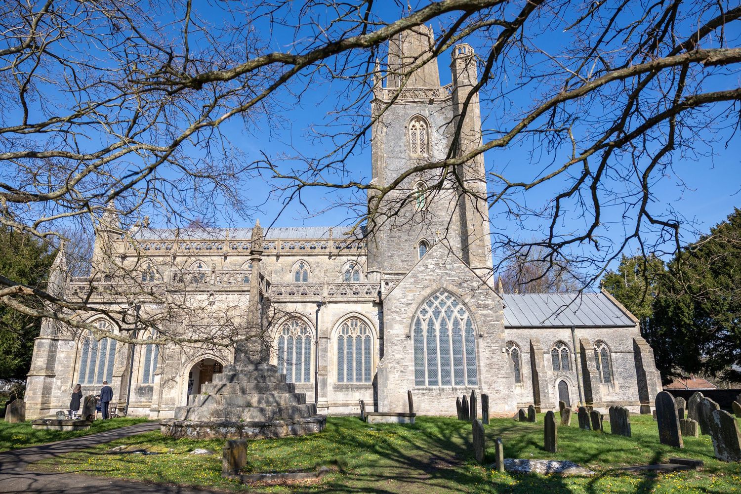 Historic stone church with Gothic architecture and stained glass windows under a bright blue sky.