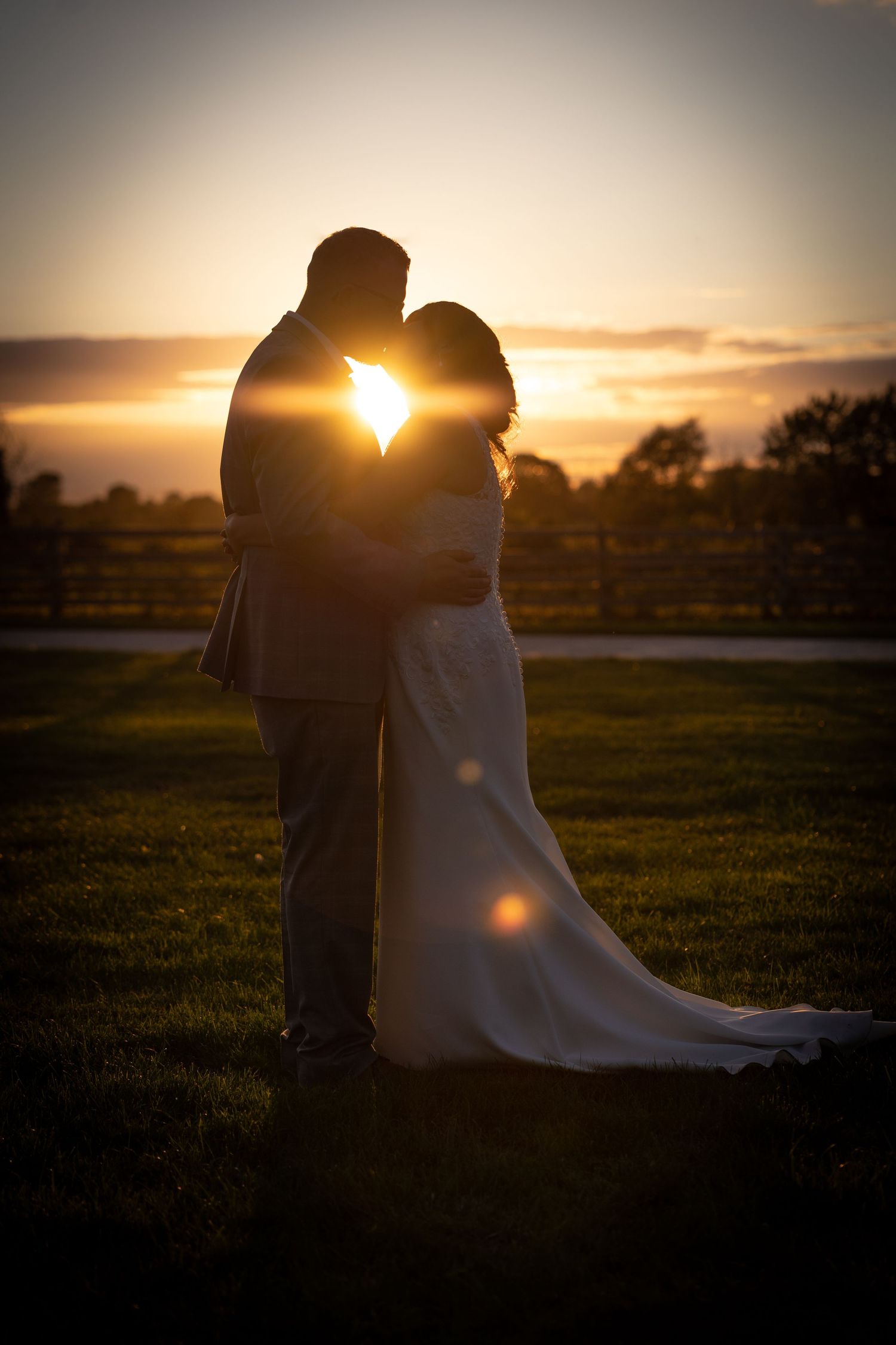 A romantic silhouette of a couple embracing at sunset, with the bride in a flowing white gown against a golden sky.