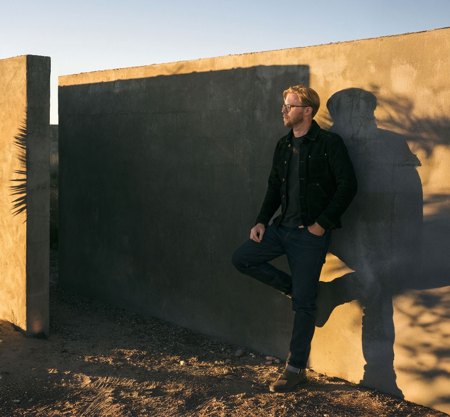 A person in black clothing walks across a wall casting long shadows during golden hour lighting.