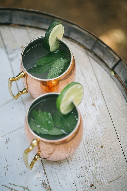 Green cocktails served in copper moscow mule mugs garnished with lime wedges.