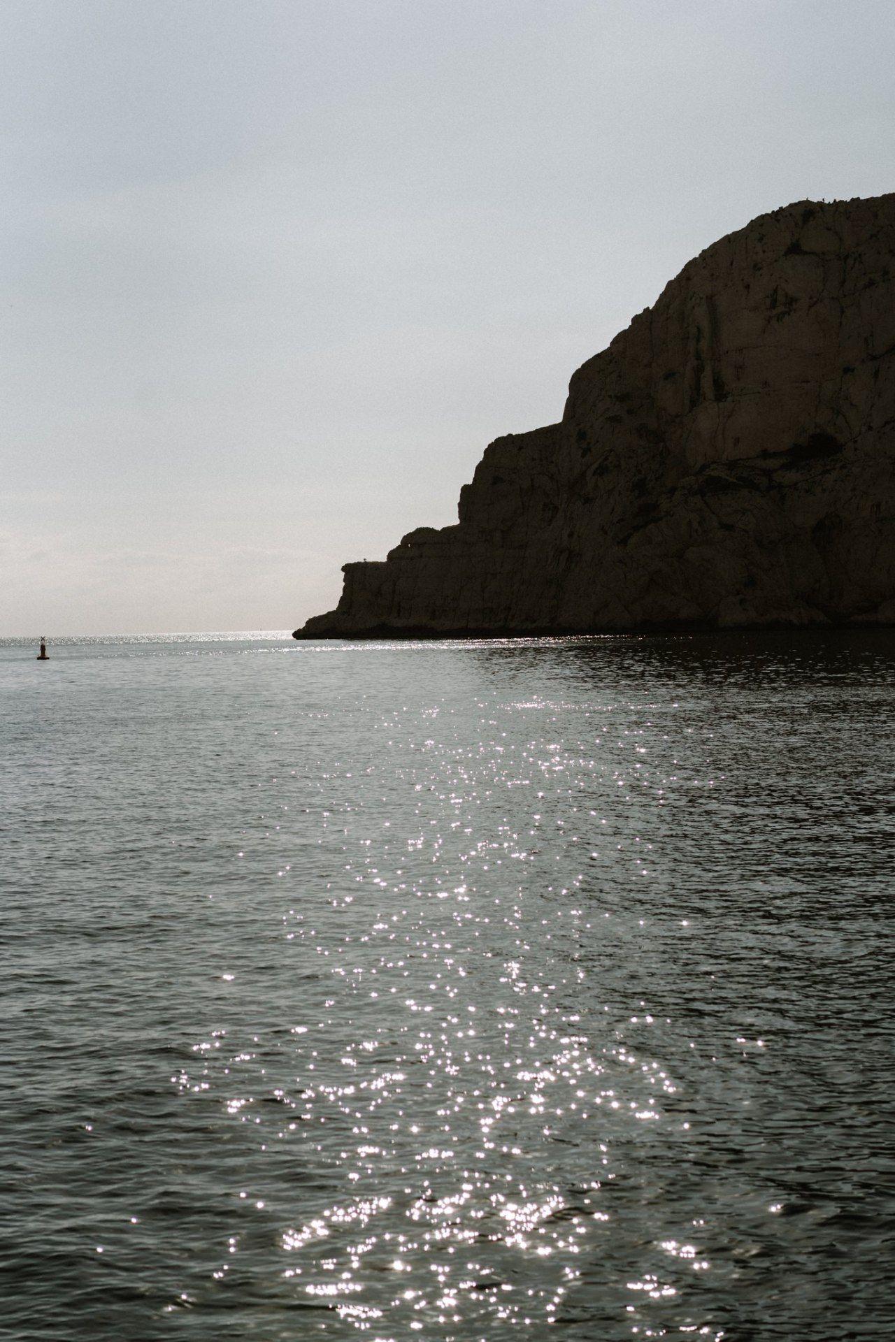 Scenic seascape with sparkling water and rocky cliffs under overcast sky.