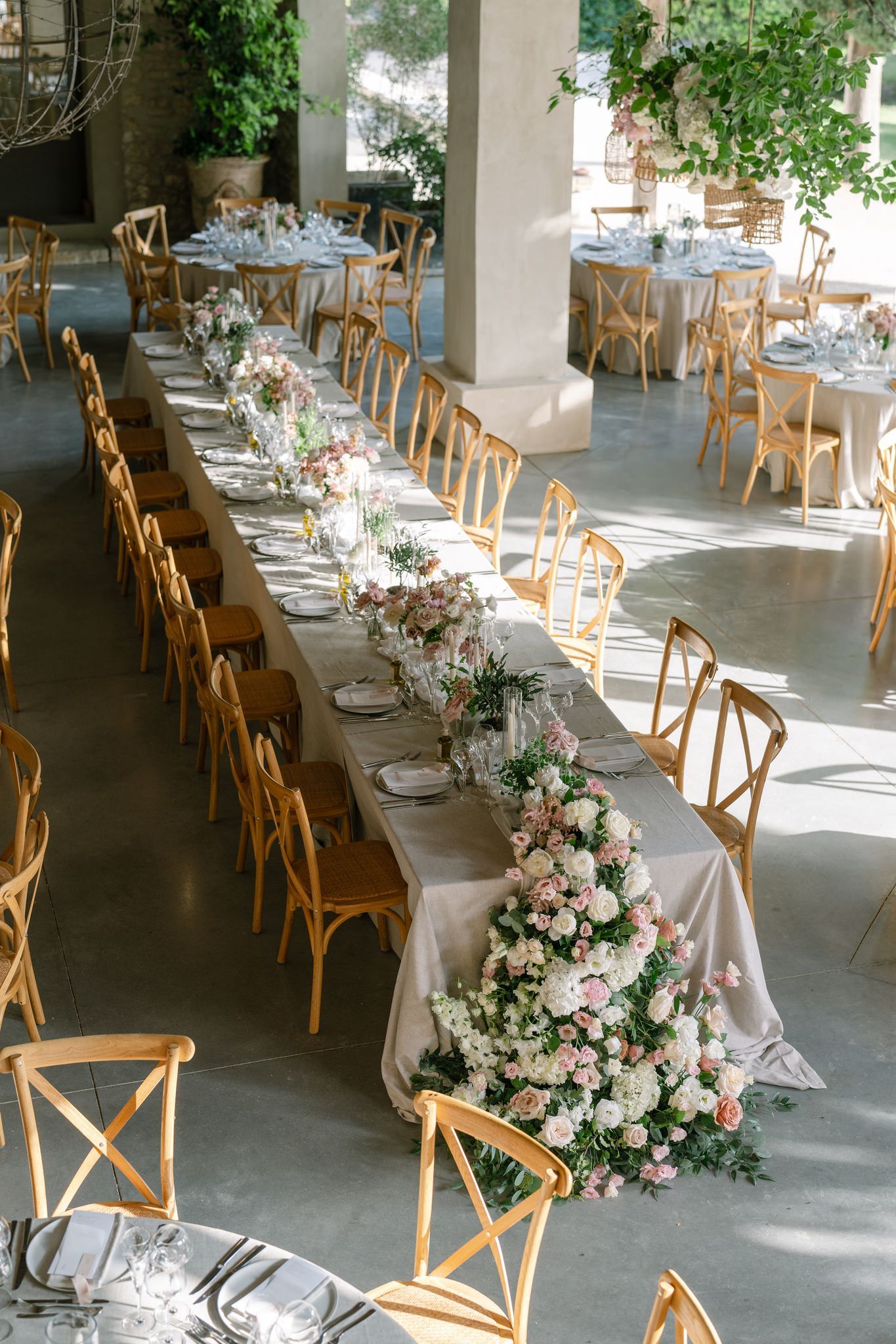 Elegant wedding reception tables with wooden chairs and lush floral arrangements in pink and white tones.