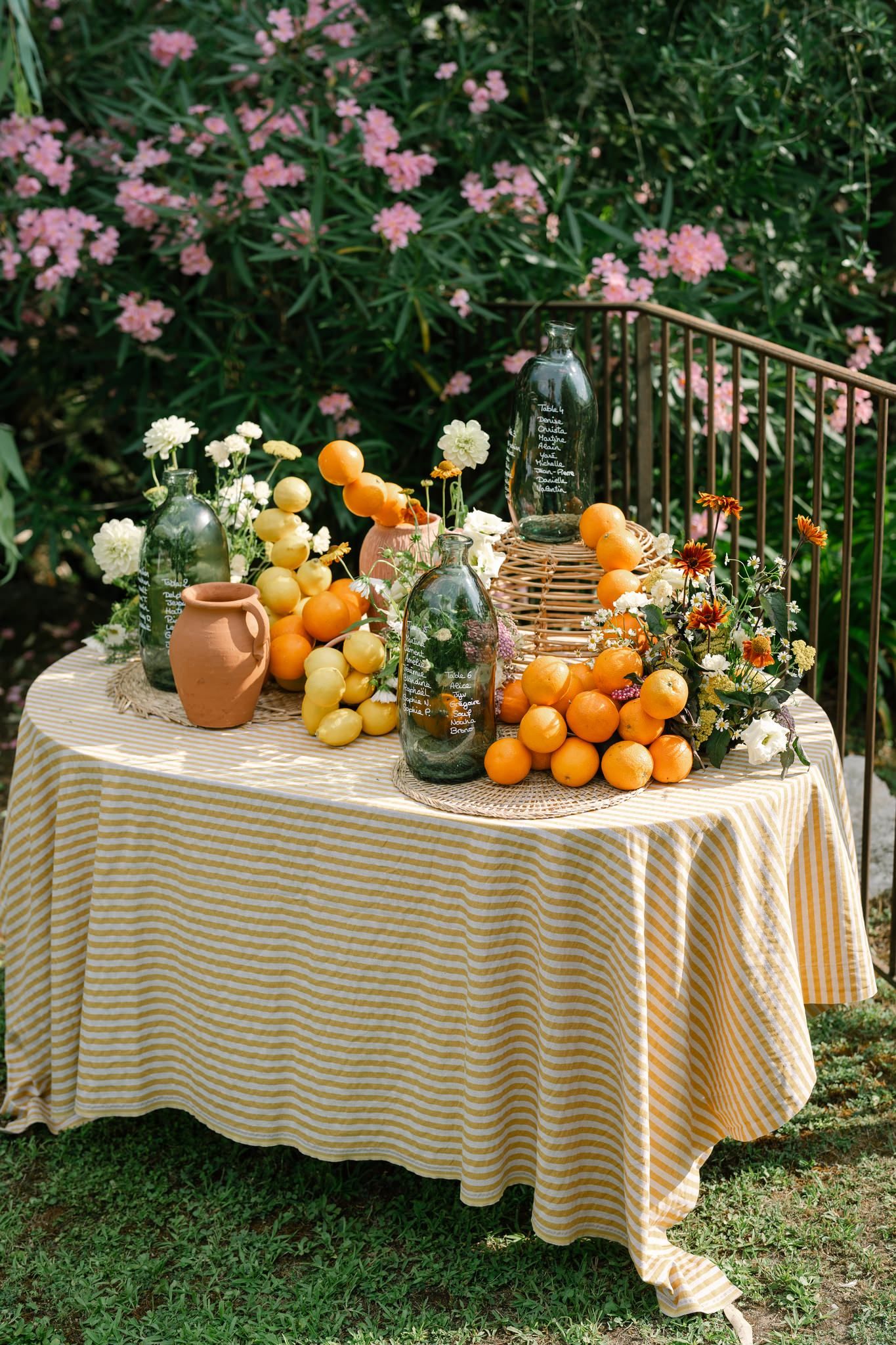 Garden table decorated with citrus fruits, flowers and vintage glassware on striped tablecloth.