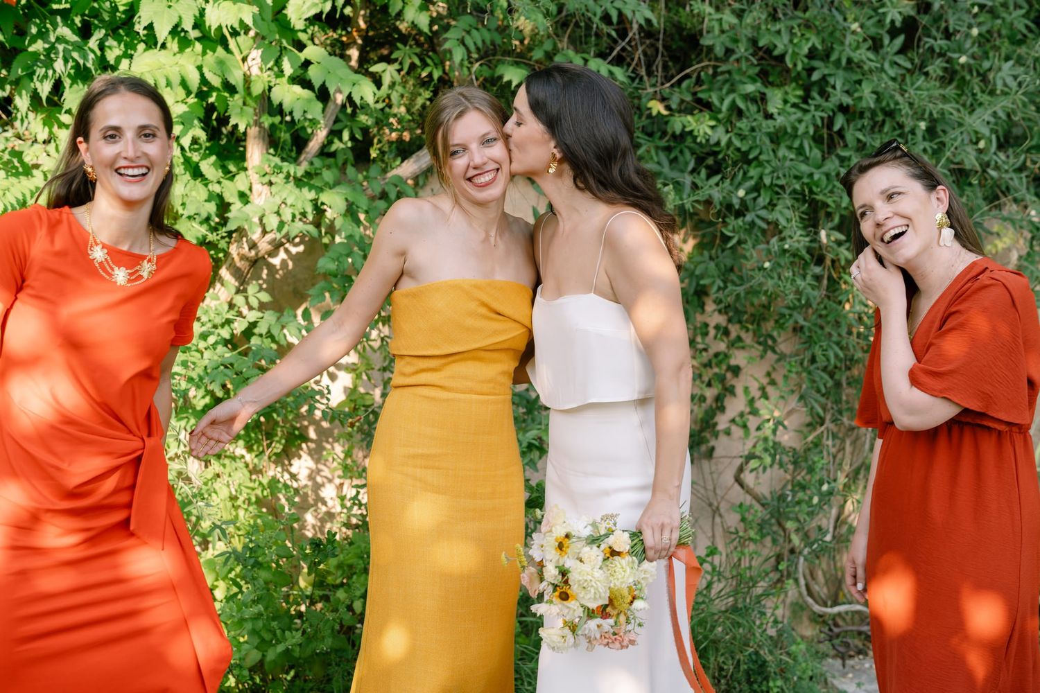 Wedding party in bright orange and yellow dresses posing outdoors.