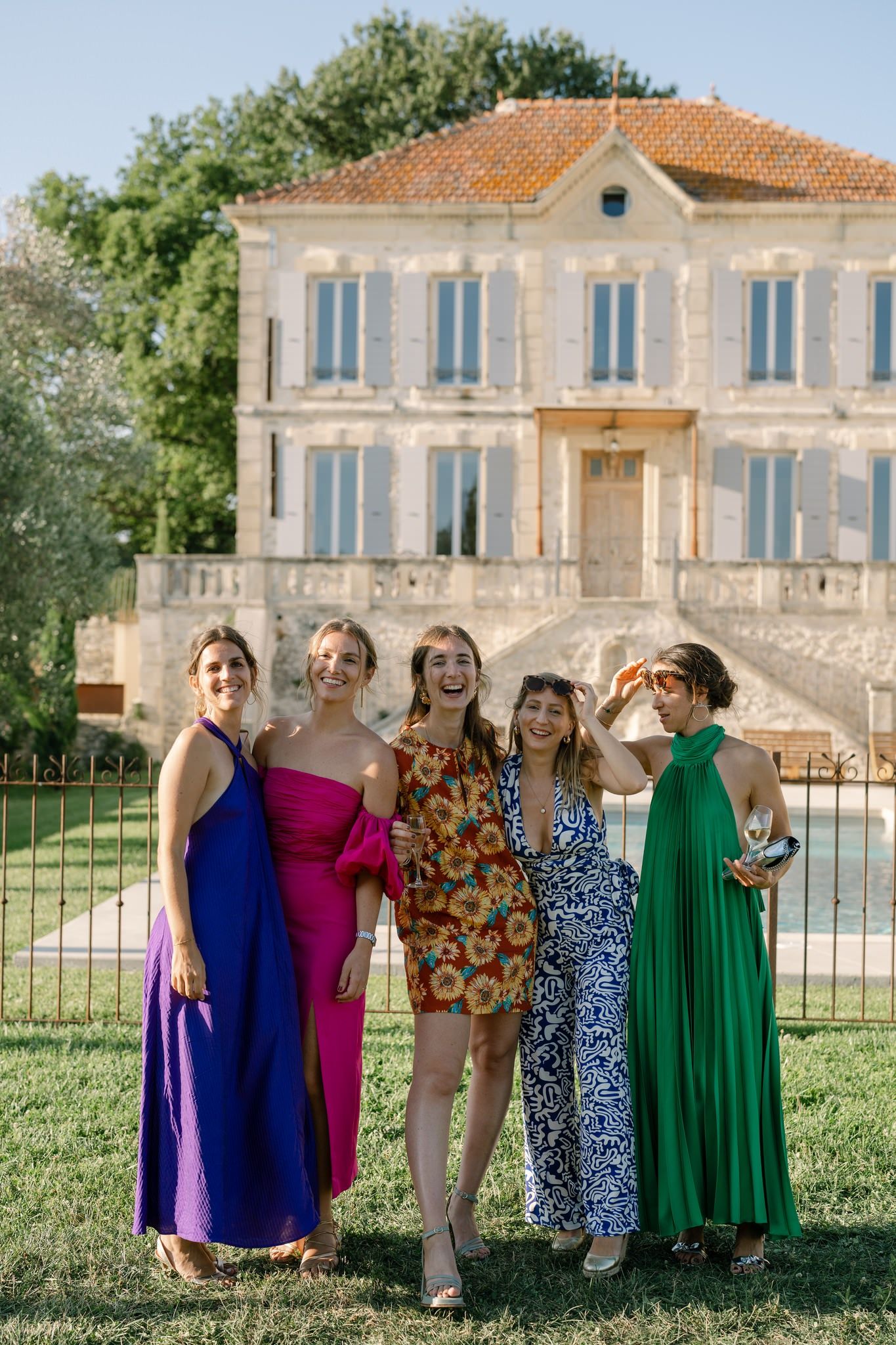 Wedding party in colorful dresses poses in front of Mediterranean style villa.