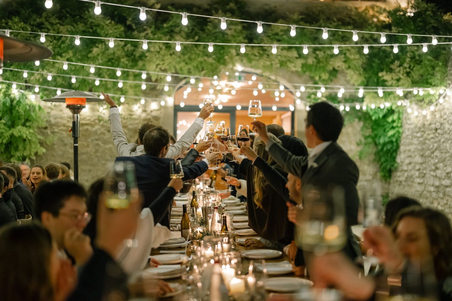 String lights illuminate an outdoor wedding reception area with stone walls and greenery.