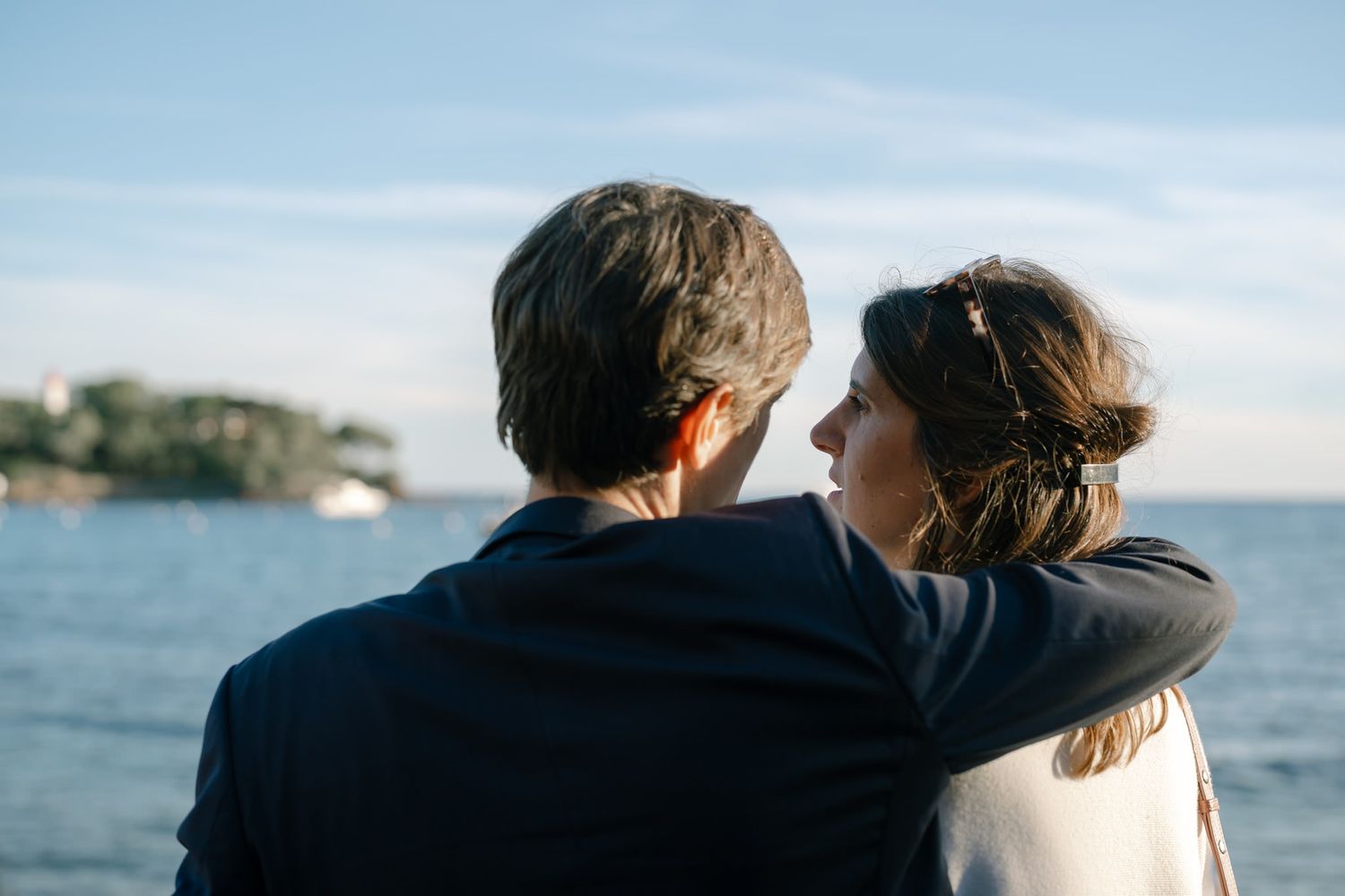 A couple walks along a scenic beach at sunset with ocean views in the background.