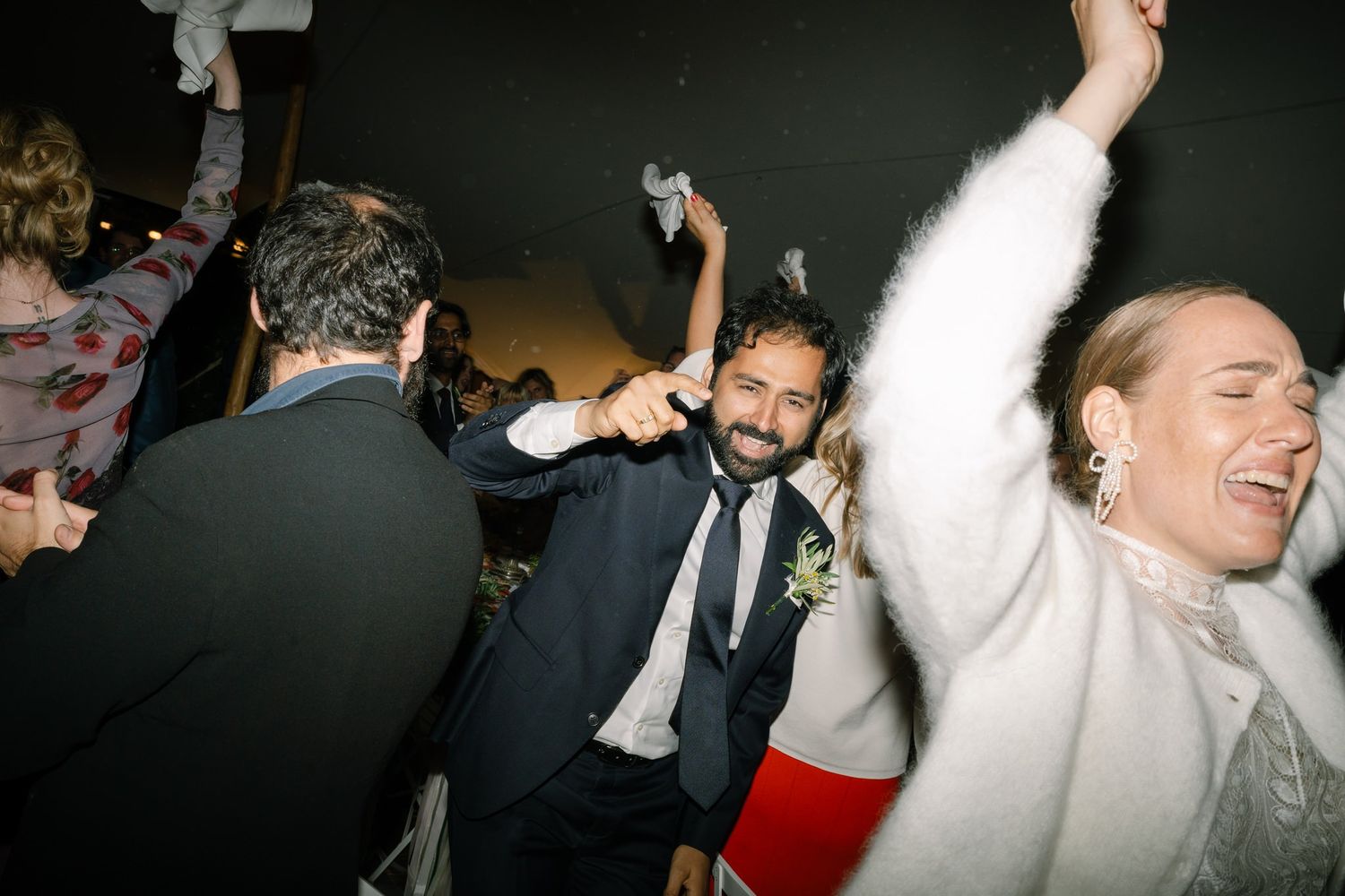 Wedding guests dancing and celebrating energetically at a lively reception party.
