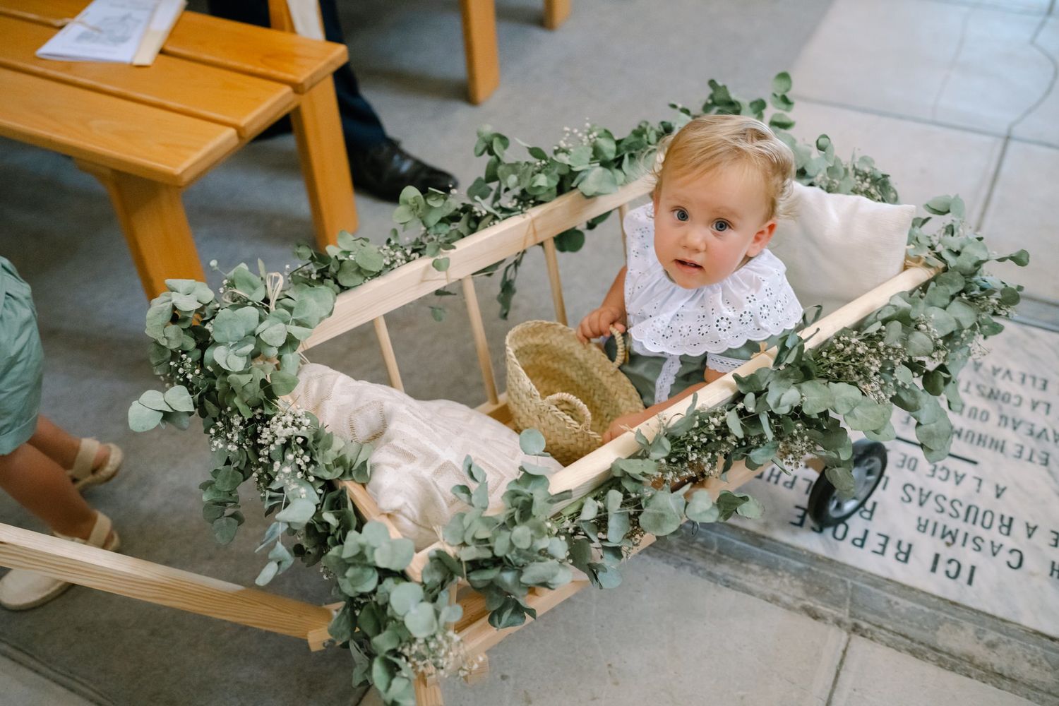 Church pews decorated with fresh greenery garlands and white floral arrangements.