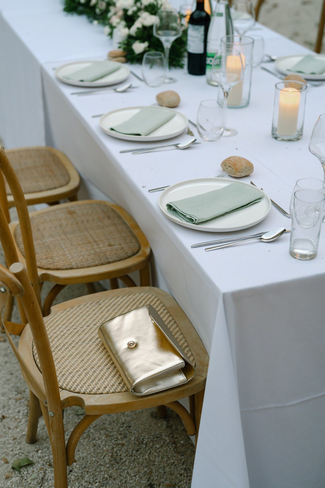 Wedding table settings with white linens and wooden cross-back chairs at an outdoor reception.