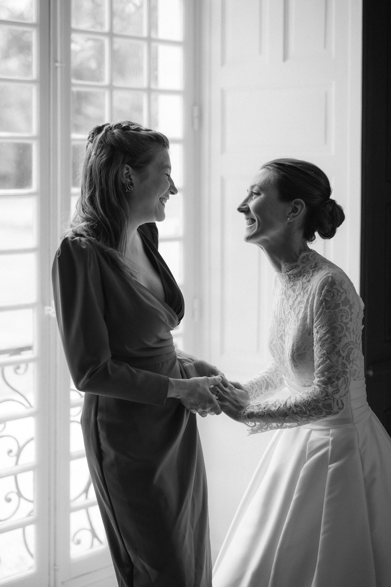 Candid moment of wedding dress preparation by a window with natural light streaming in.