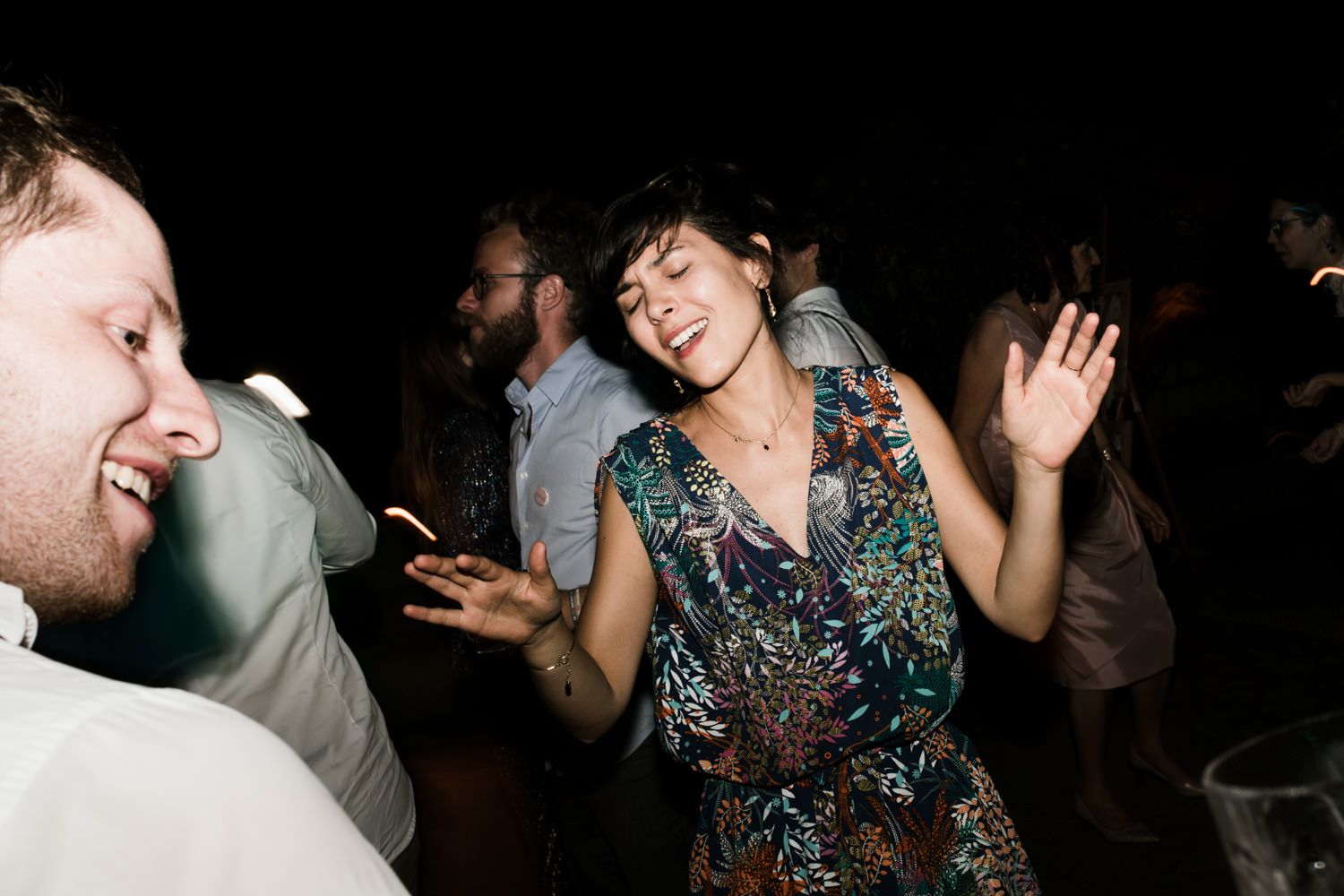 Guests dancing and mingling at an evening celebration with dark ambient lighting.