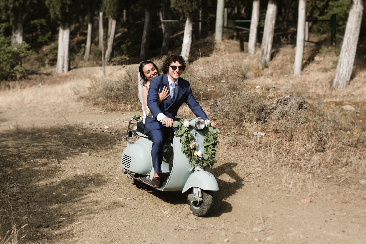 Couple riding vintage Vespa scooter through rustic countryside.