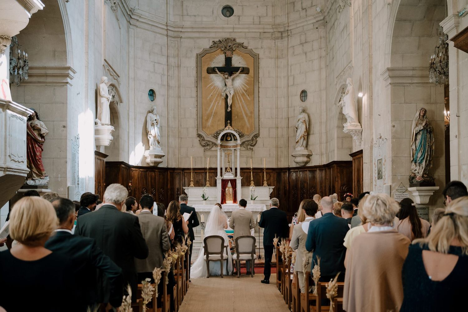 Interior of a historic Catholic church with white stone walls and religious statues during a wedding.