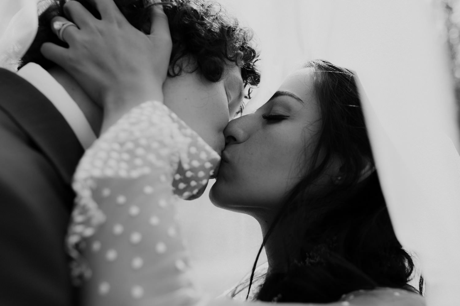 Romantic close-up shot of a couple sharing a kiss under a delicate veil.
