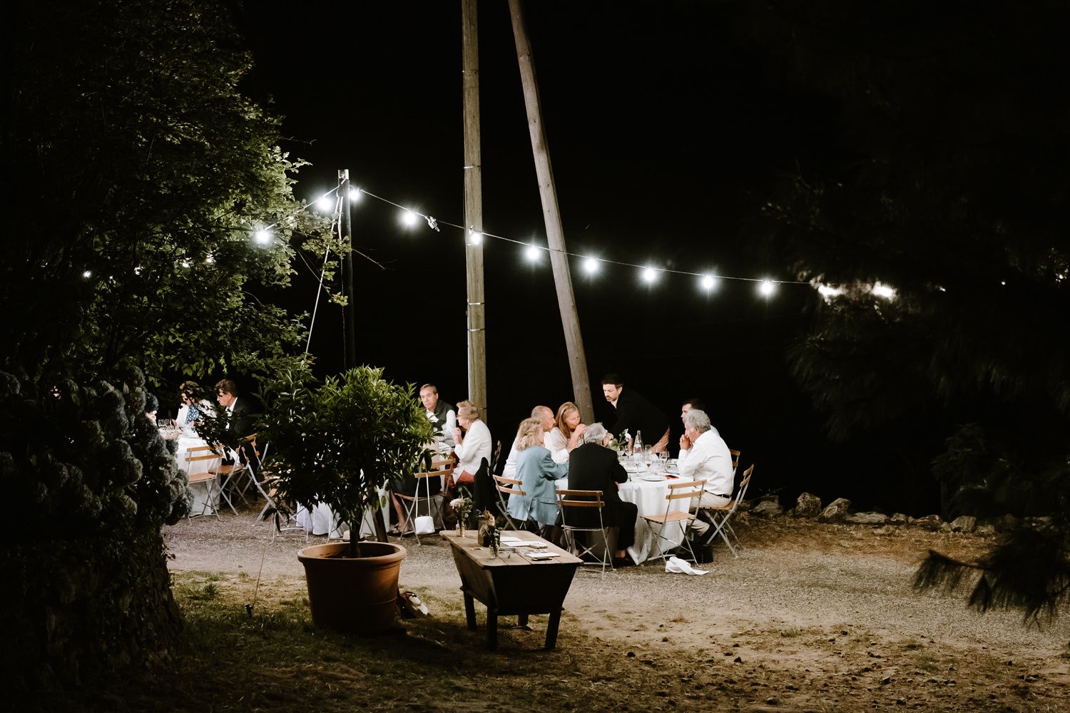 Nighttime outdoor reception with string lights illuminating guests seated at tables.
