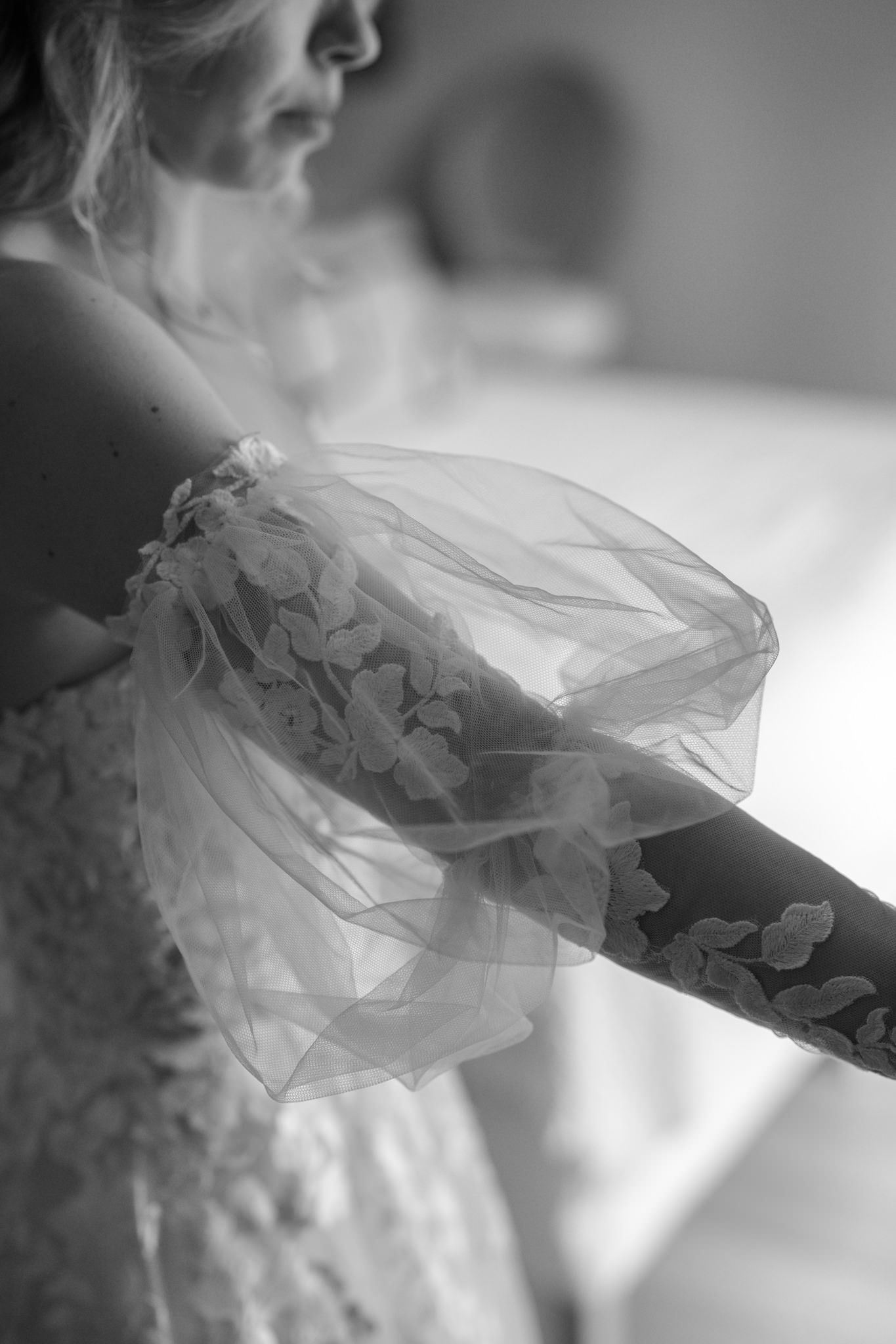 Close-up detail of a wedding dress showing intricate lace appliques and flowing tulle fabric.